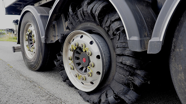 A shredded truck tire on a truck stopped at the side of road.