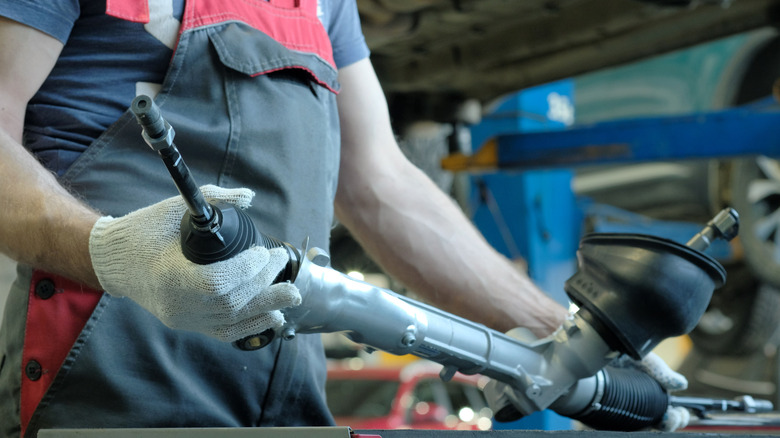 A mechanic holding a rack and pinion steering system in hands.