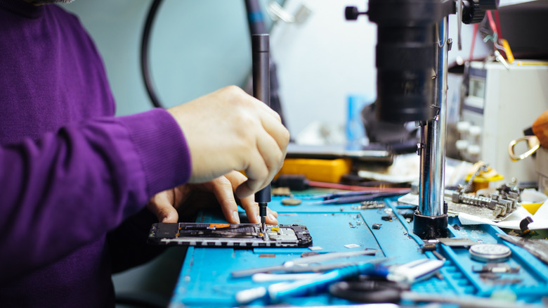 Technician disassembling smartphone with screwdriver.