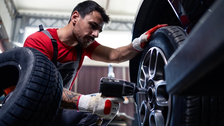 Male mechanic removing wheel lugs with impact wrench