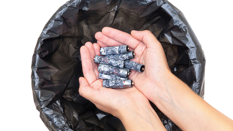 A person holding corroded batteries over a trash can.