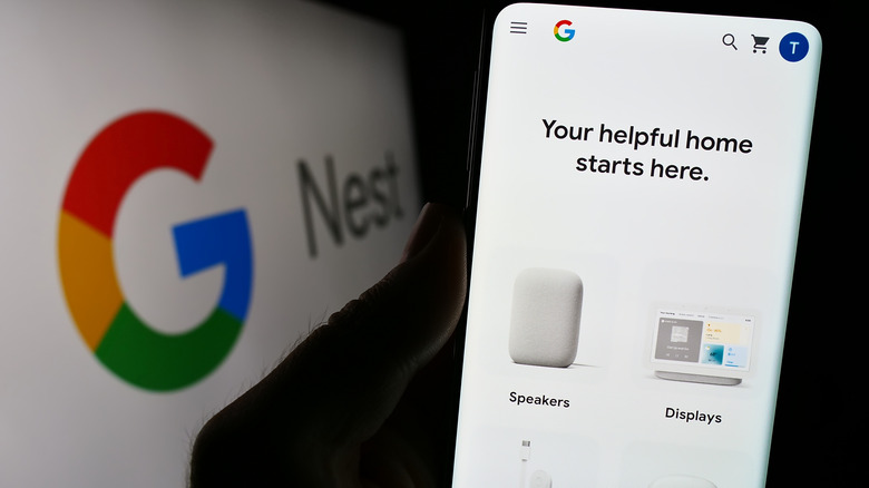 A hand holding a phone showing the devices listed on the Google Home app while the Google Nest logo is on display at the back.