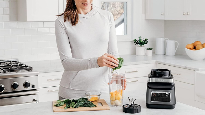 A person preparing a smoothie using a Ninja blender in a kitchen
