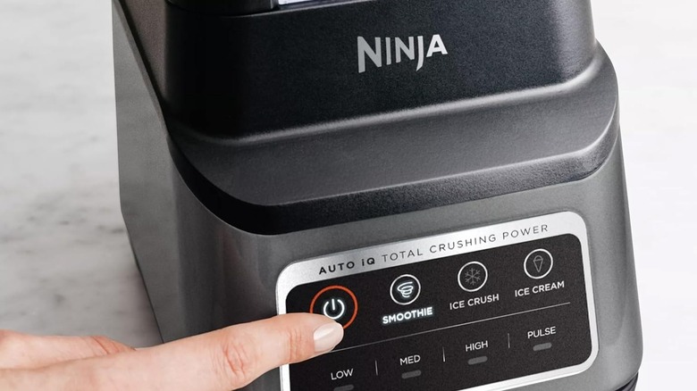 A person pressing a Ninja blender's power button with LED indicator