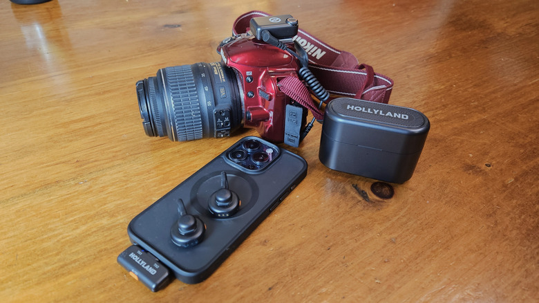 Hollyland Lark M2S along with a black iPhone 15 Pro and a red DSLR camera.