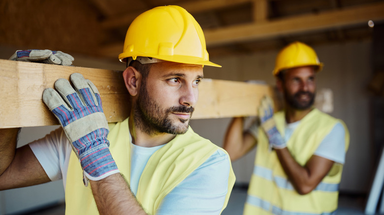Two men carrying wooden beam on construction site