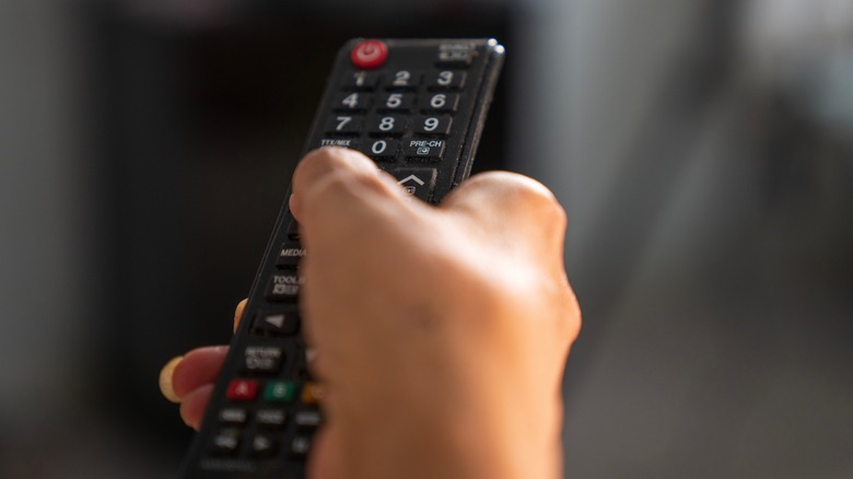 A hand holding up a TV remote against a blurred background