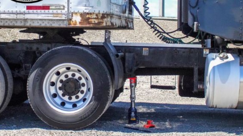 A bottle jack being used to lift semi-truck's trailer.