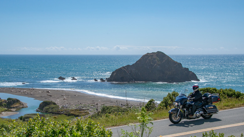 Motorcyclist on Pacific Coast Highway with ocean and large rock in background