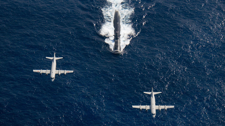 Two aircraft flying over a surfaced submarine