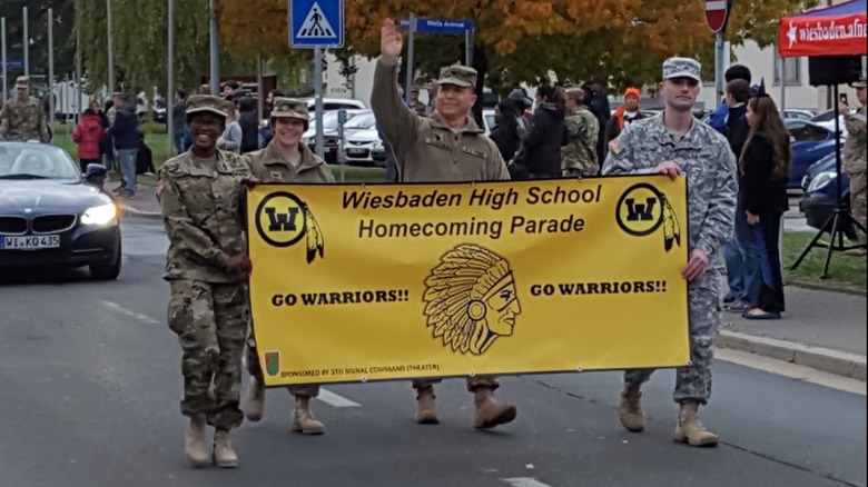 Four American soldiers in Germany carry a banner for Wiesbaden High School in a parade.