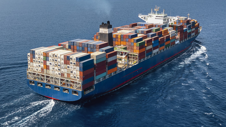 A large container cargo ship travels over calm, blue ocean.