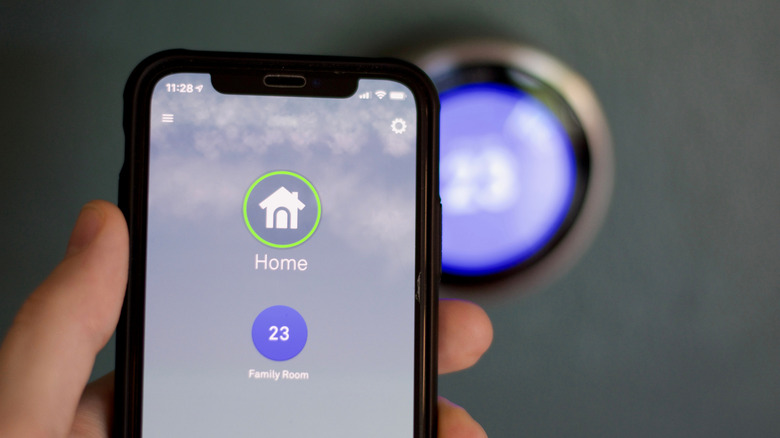 Person using cell phone to adjust temperature on smart thermostat