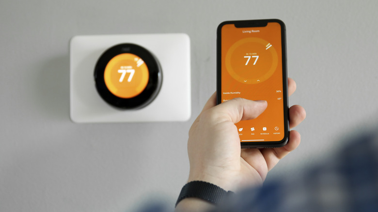 Man using cell phone with smart thermostat