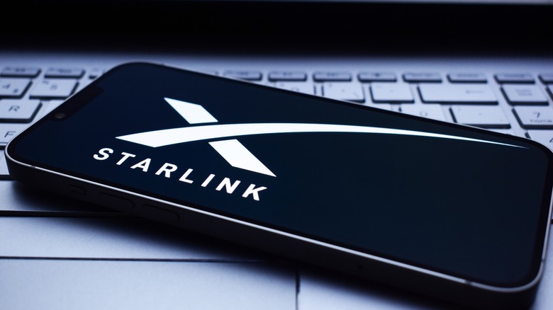 Smartphone on a laptop keyboard showing the Starlink logo