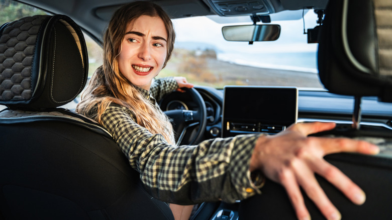 A young focused woman is parking in reverse at the wheel of a modern car.