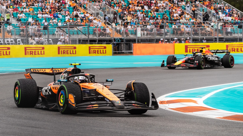 Lando Norris driving his McLaren F1 car around a corner with a Red Bull in the background