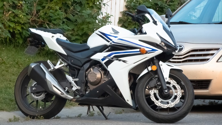 A white Honda CBR500R motorcycle parked beside a car