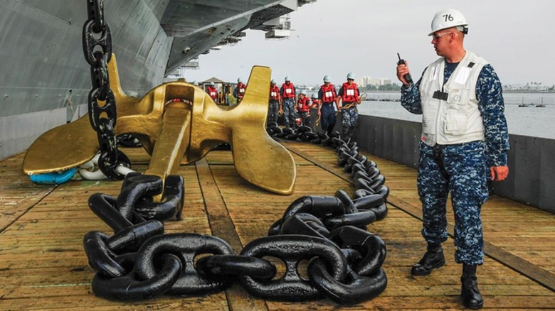 A sailor standing beside an aircraft carrier anchor and several chain links