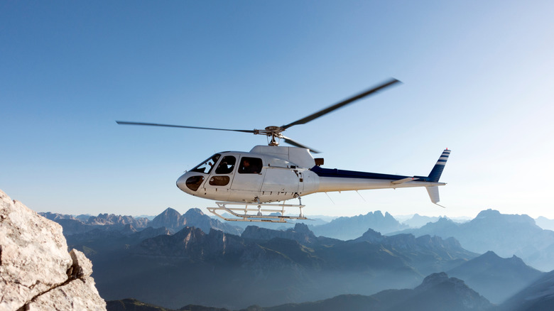 A white helicopter flying above some mountains