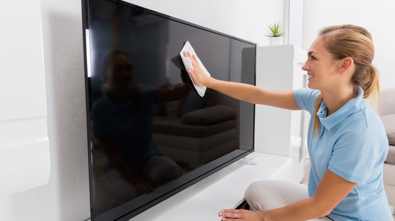 Young woman wiping TV screen with cloth