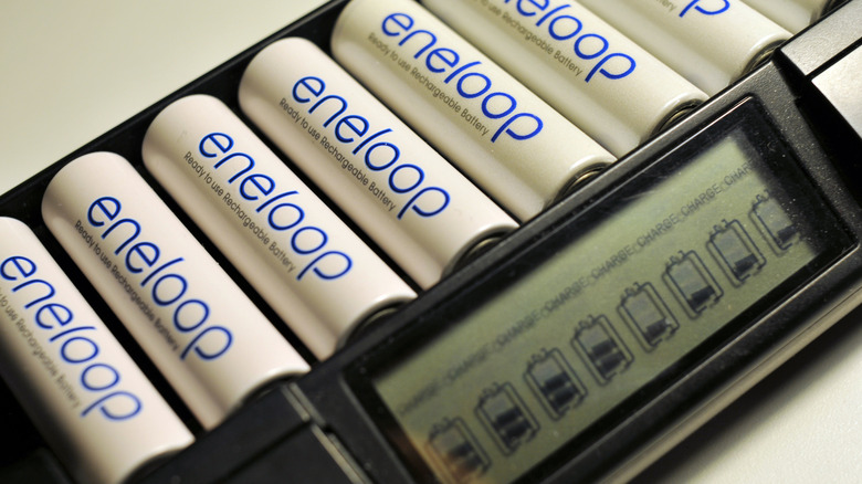 eneloop batteries in an eneloop chargere. The batteries are white with blue writing and say "eneloop - ready to use rechargeable battery"