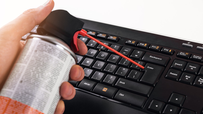 Person spraying compressed air at a computer keyboard