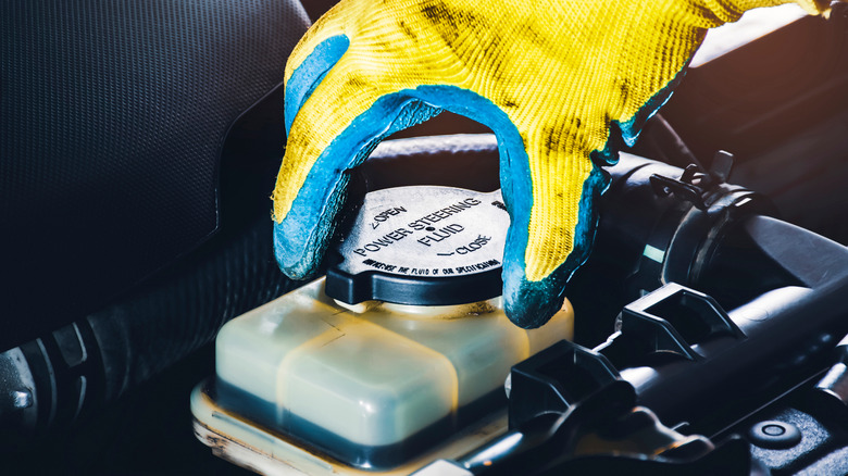 Mechanic's gloved hand opening power steering fluid reservoir in car's engine bay
