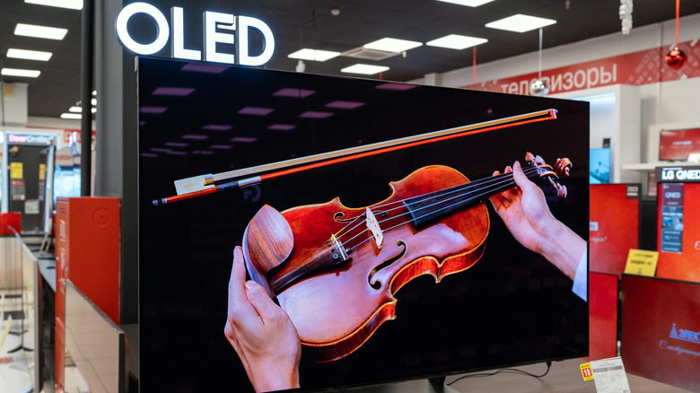 LG OLED TV in a store, displaying a person holding a cello, OLED branding above
