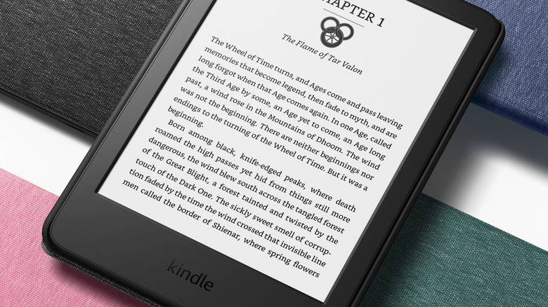 A novel displayed on an Amazon Kindle with black, blue, pink, and green Kindle covers in the background
