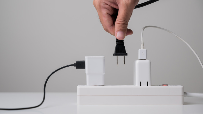 A hand holding a plug over a power strip