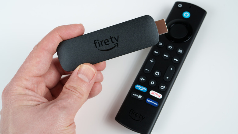 Person holding a Fire TV Stick with a remote on a table