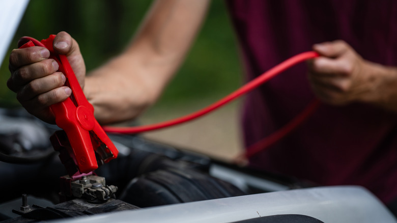 Person attaching jumper cables to car battery