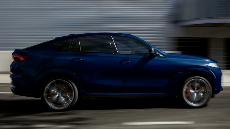 BMW X6 M60i driving down city street with a building in the background