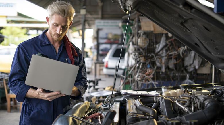 Auto Mechanic using a computer for problem searching the engine of a car.