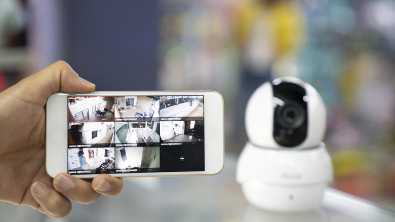 A Person's Hand Holding Mobile Phone With CCTV Camera Footage On Screen
