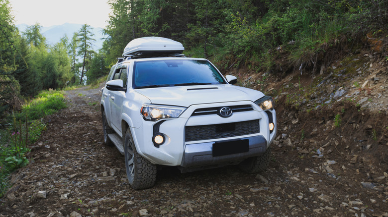 Front 3/4 view of a fifth gen Toyota 4Runner in white going up a muddy trail, white roof box attached