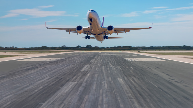 Airport runway with rubber markings in landing zone, with aircraft on final approach and flaring for landing