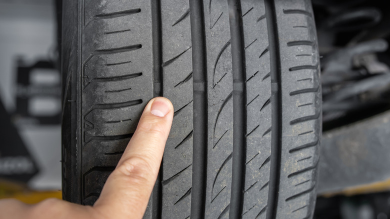 Person pointing at the tread on an old tire