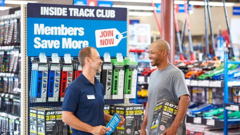 A Harbor Freight employee assists a customer in front of an sign for the Inside Track Club