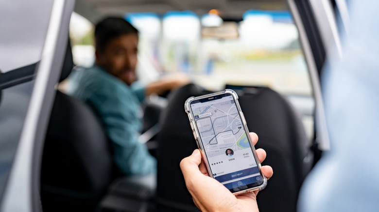 A person entering an Uber, holding a phone with the Uber app open, with the driver blurred in the background