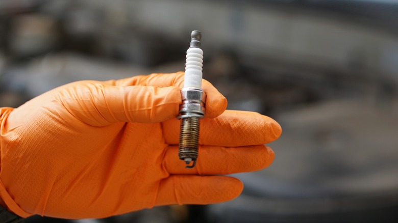 An orange gloved hand holding an old spark plug