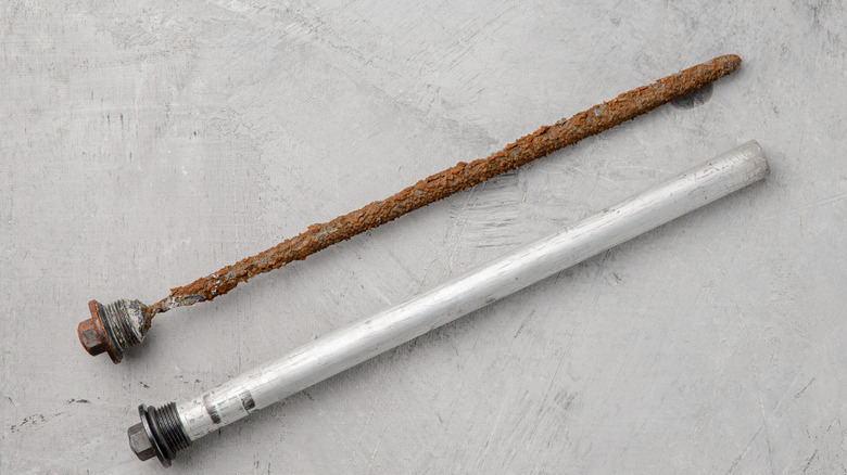 New and worn magnesium anodes of a water heater side by side on cement