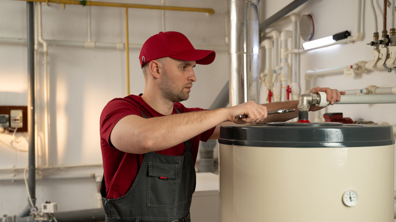 Man in red shirt and cap attaching pipe to top of water heater with wrench