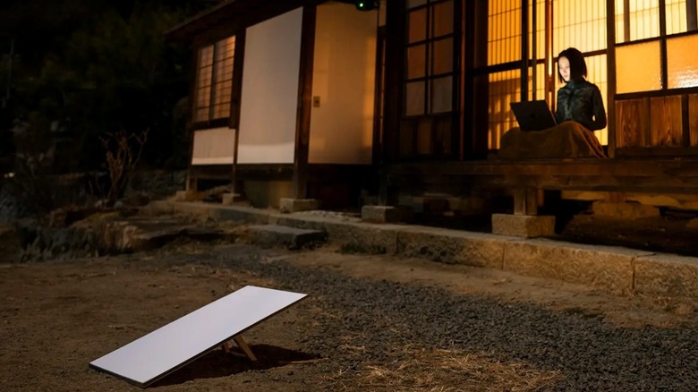 A young woman uses Starlink to access the internet from a cabin porch.