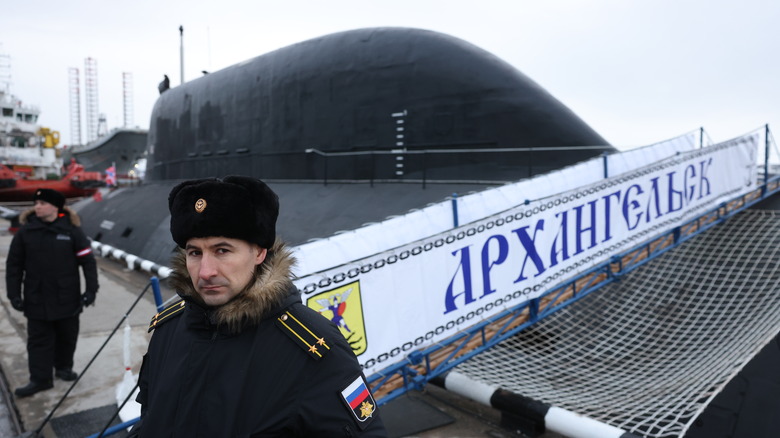 Russian naval officers walk past the Arkhangelsk K-564 Yasen-class submarine at a nuclear submarine base