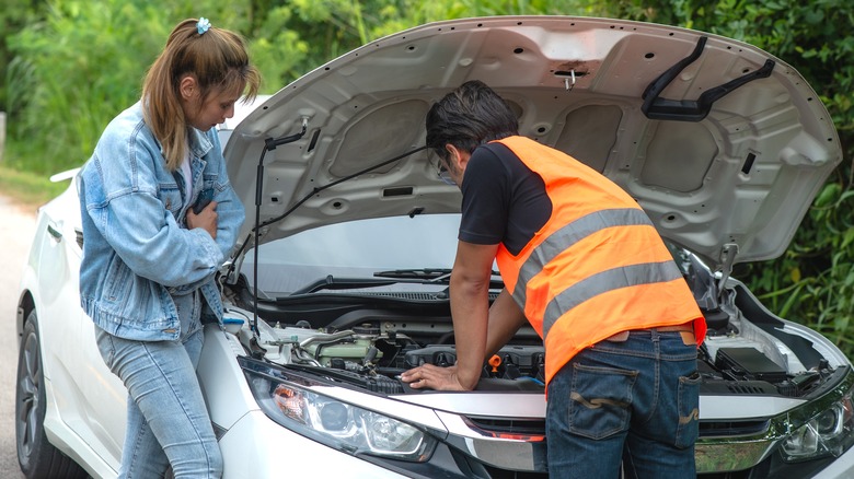 Car mechanic fixing open hood breakdown vehicle for a person on the road