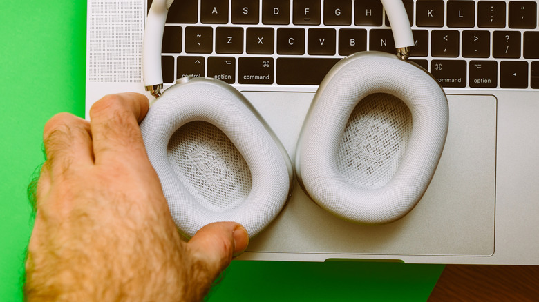 Person removing AirPods Max ear cups kept on a MacBook