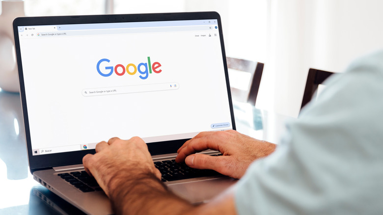 An open laptop displaying the Google new tab page on the Chrome browser. There are two hands typing on the keyboard laptop.