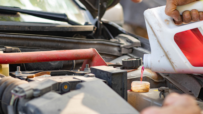 A man's hand is shown pouring pink antifreeze into a vehicle